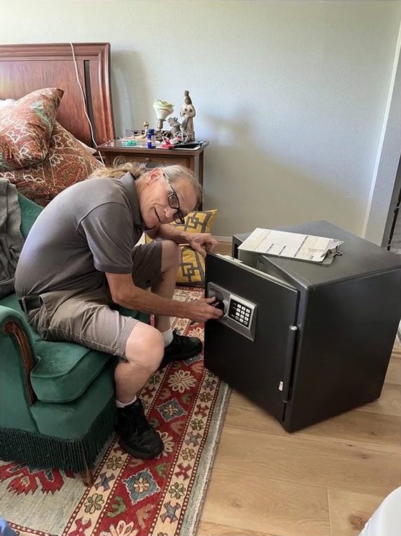 Jack Mathes, owner of ABC Lock and Safe, kneeling beside a small safe he is working on in a living room