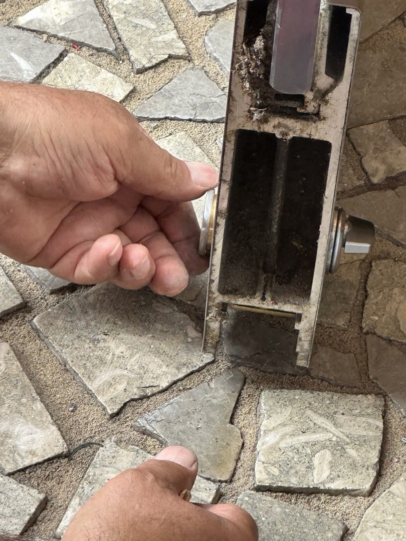 A locksmith holding a storefront door lock body over a stone floor during a repair