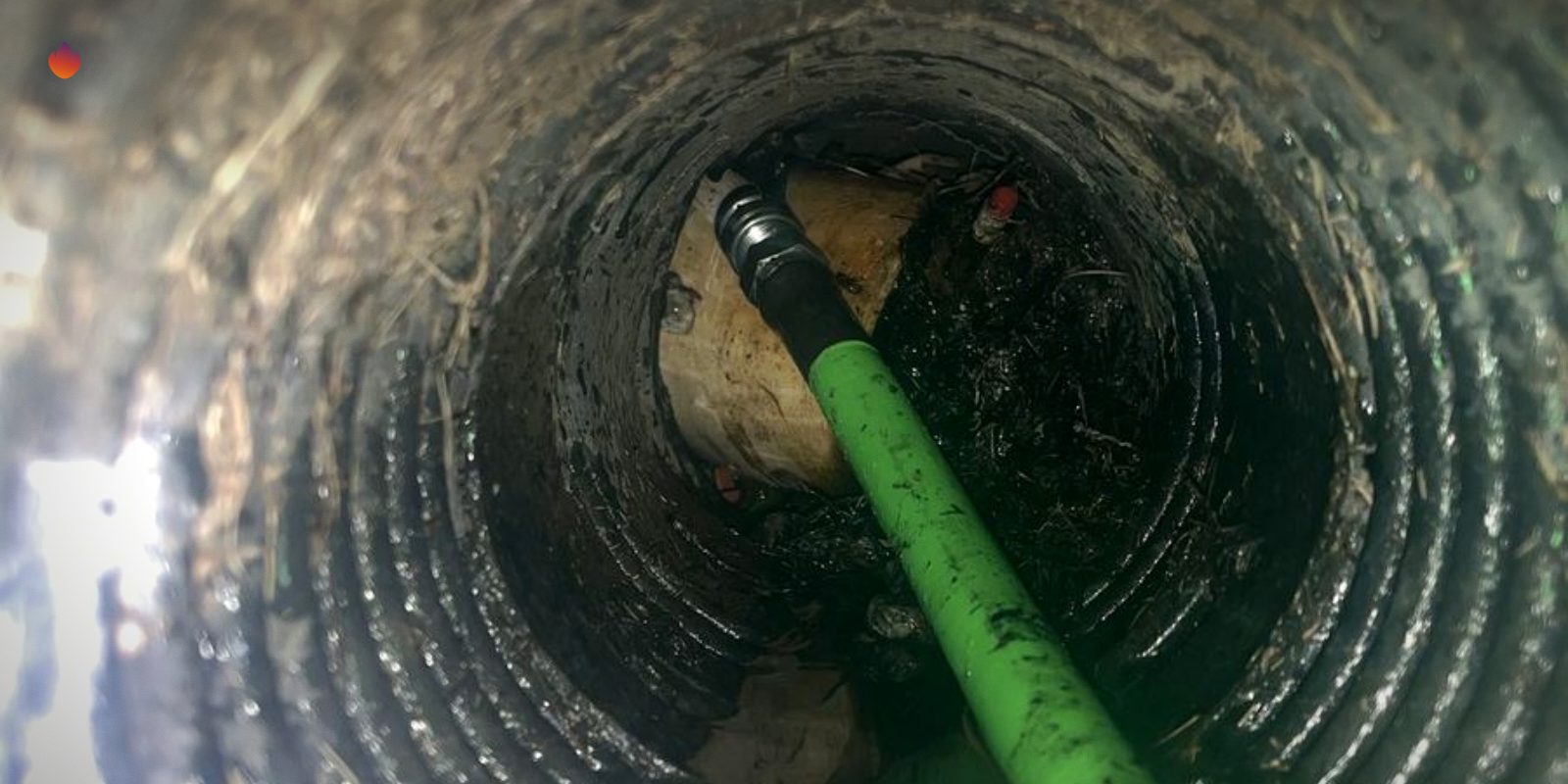 A camera view down a sewer line with a green camera cable in the pipe