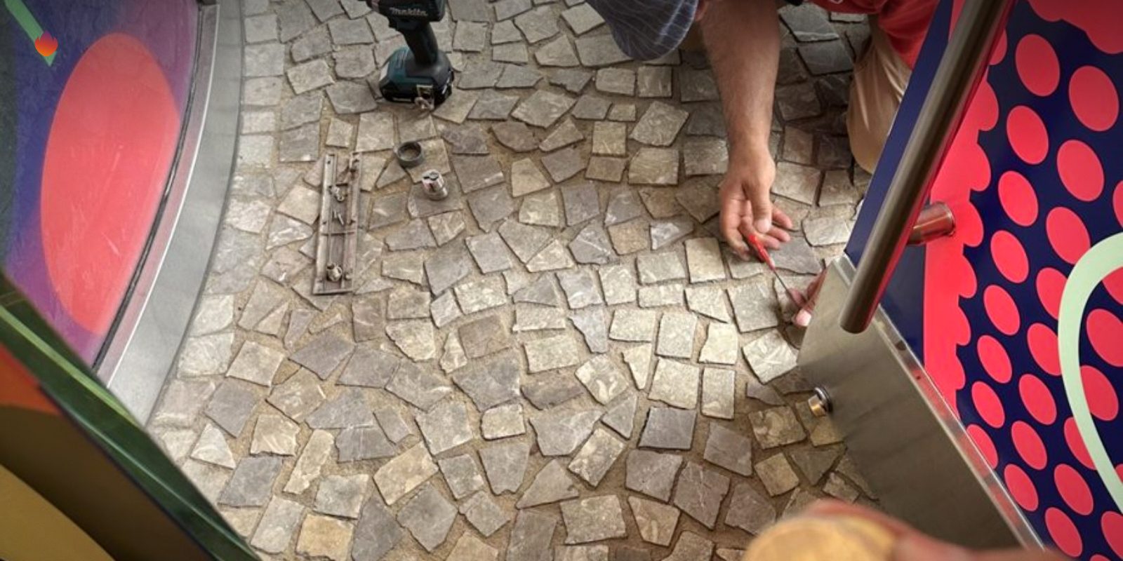 A locksmith holding a lock cylinder over a stone floor at a storefront job