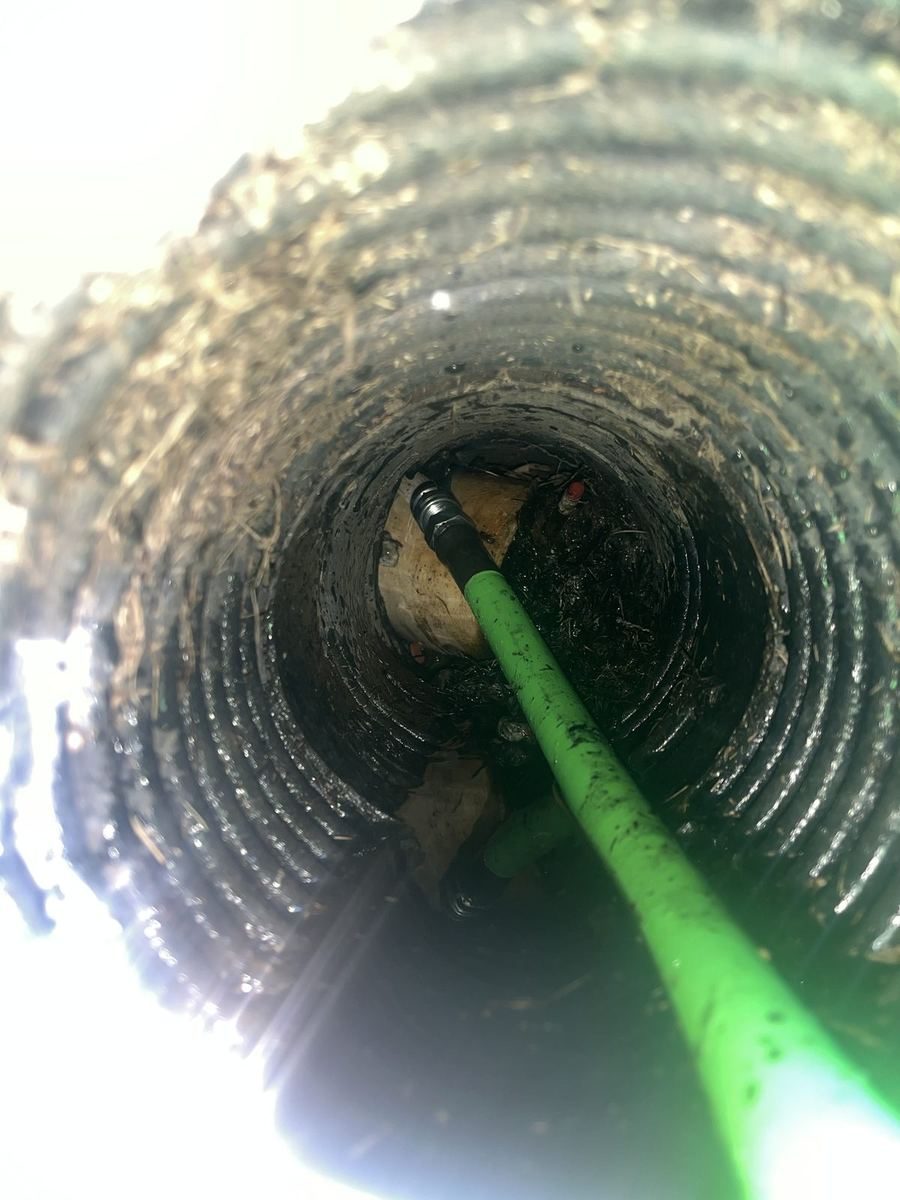 Camera view down a sewer line, with a green camera cable running into the pipe