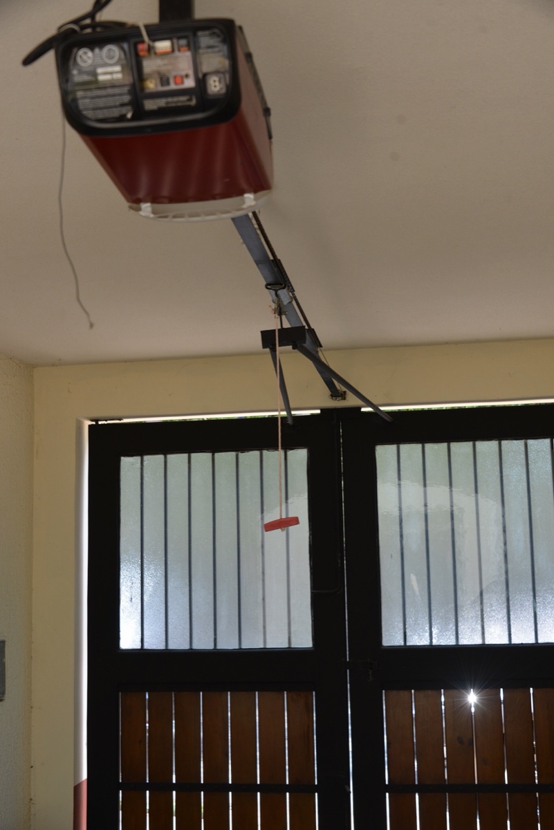 A ceiling mounted garage door opener with its rail running to the top of a closed wood and glass door