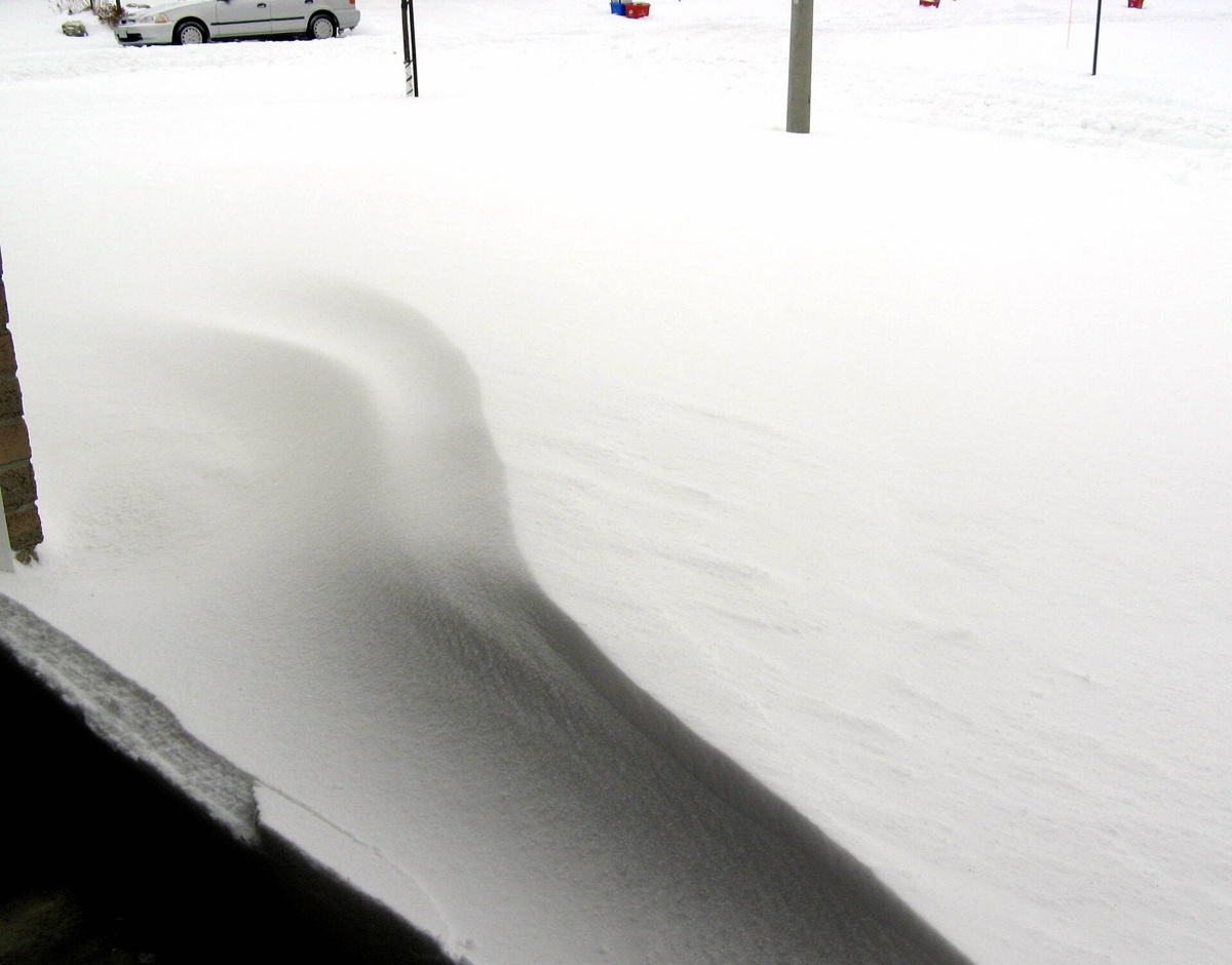 A snow drift piled across a driveway, seen from inside an open garage door