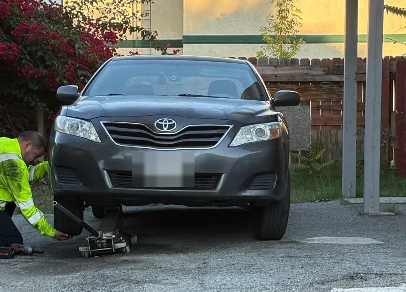 A Hemet Mobile Mechanic tech jacking up a sedan in a San Jacinto driveway