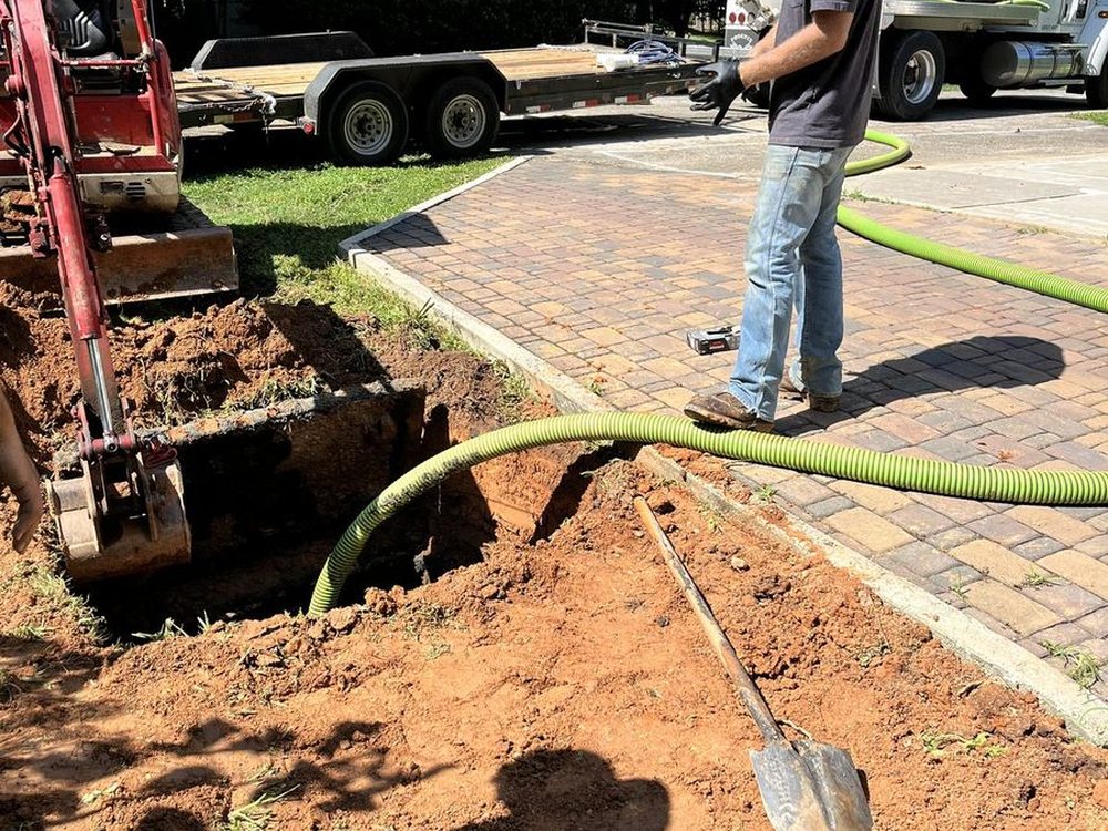 A septic tech pumping out a tank in a customer's yard, the hose running back to the truck