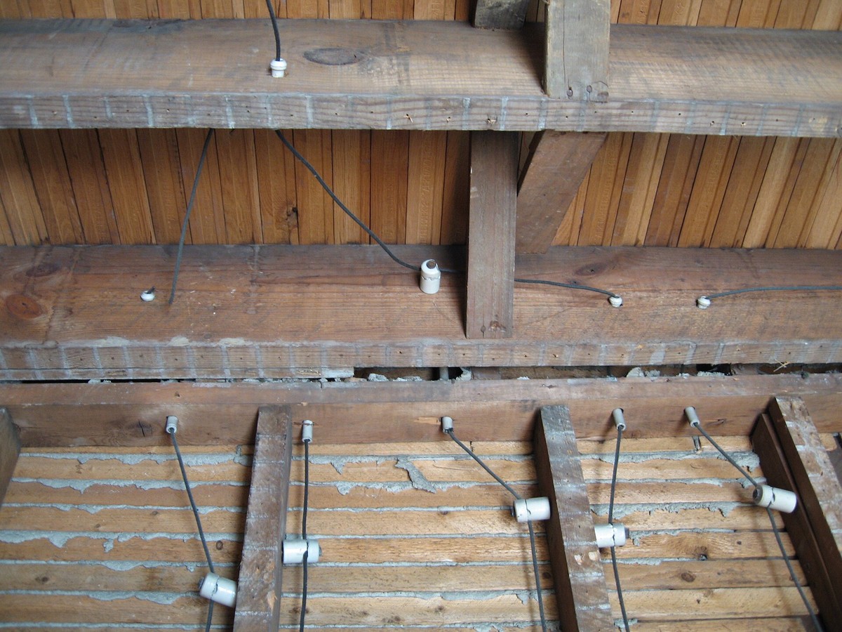 Old knob and tube wiring running along wood joists in an attic, single wires held on white ceramic knobs