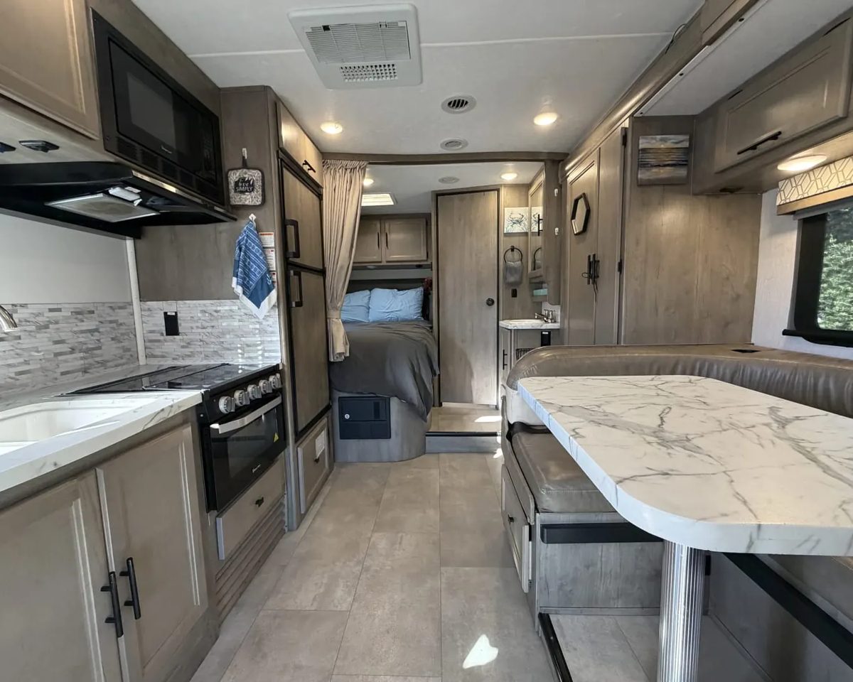 Inside a Coachmen Prism motorhome after a turnover, with a clean galley, dinette and bed