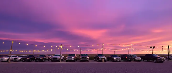 Row of used pickups and SUVs on a small lot under a West Texas dusk sky