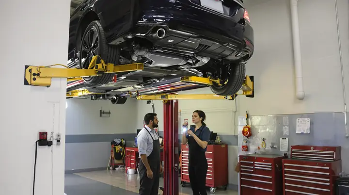 Mechanic showing a buyer the underside of a used sedan on a lift
