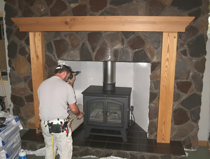 Two installers sliding a new insert into a lava rock fireplace with a stainless liner above