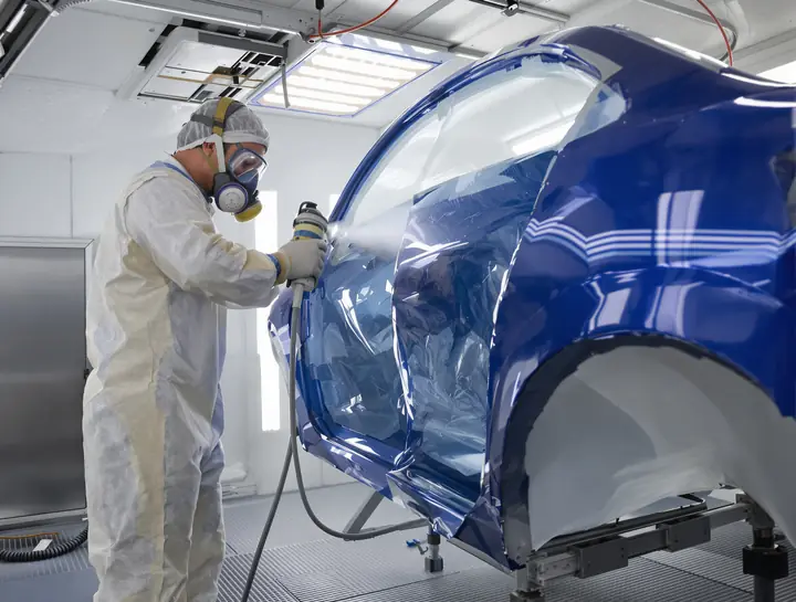 Painter spraying blue base coat on a door in the paint booth