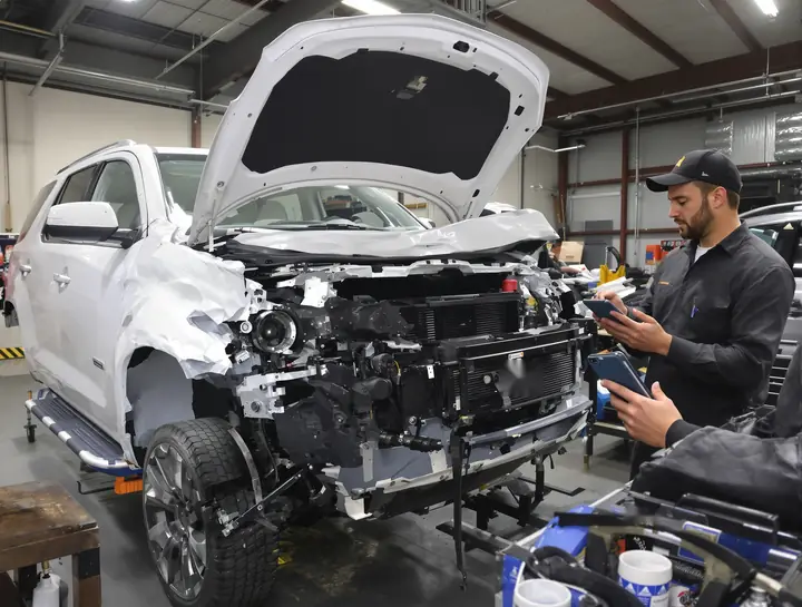 Techs taking photos of hidden damage after pulling the bumper off a white SUV
