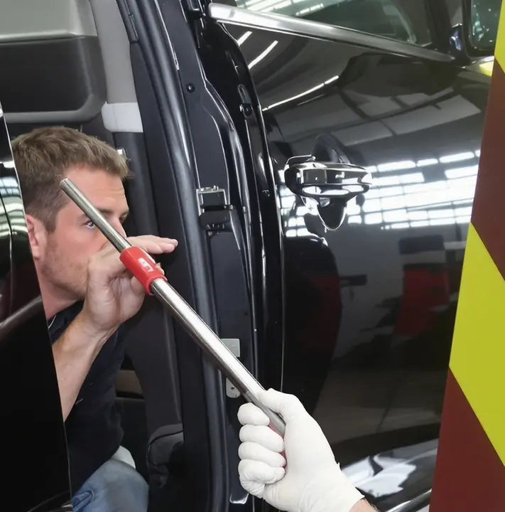 Paintless dent repair on a black SUV door using a steel rod and line board