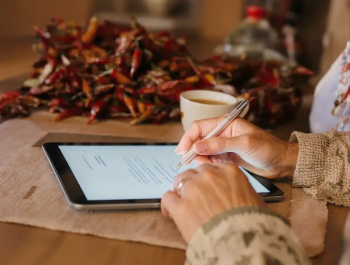 An older woman signing cremation papers on a tablet at her kitchen table