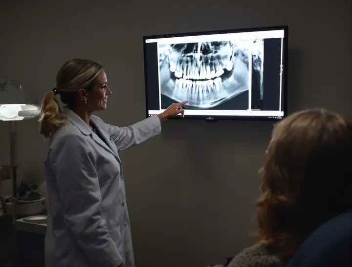 Dentist pointing at a panoramic x ray while a patient listens