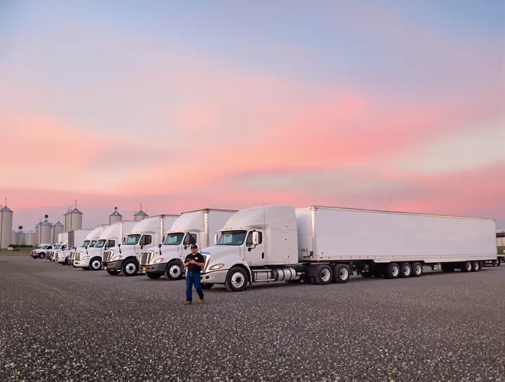 Mechanic walking a line of box trucks in a fleet yard at sunrise