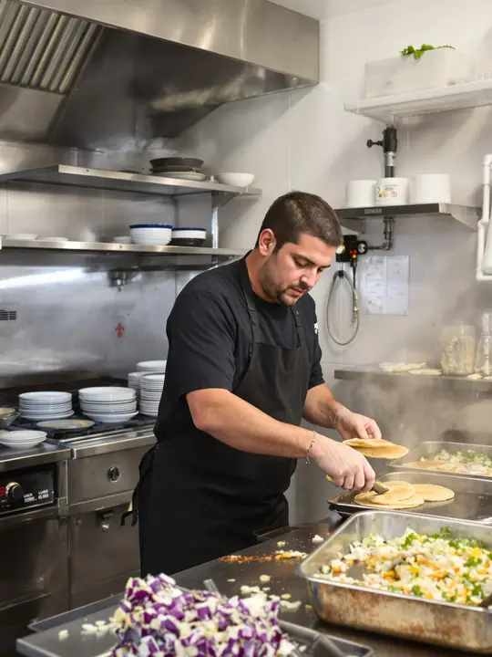 A line cook plating tacos late in a long shift in Fruitvale