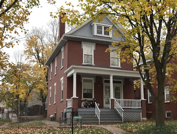A brother and sister talking on the porch steps of their parents' brick house in autumn