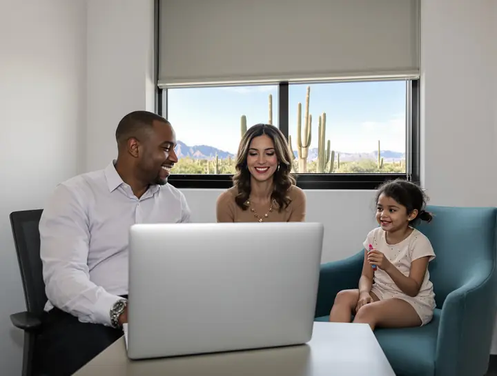 A father and his lawyer smiling at a laptop while his daughter sits in an armchair