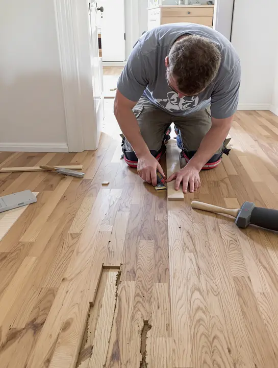 Carpenter weaving new oak boards into an old floor near a kitchen doorway