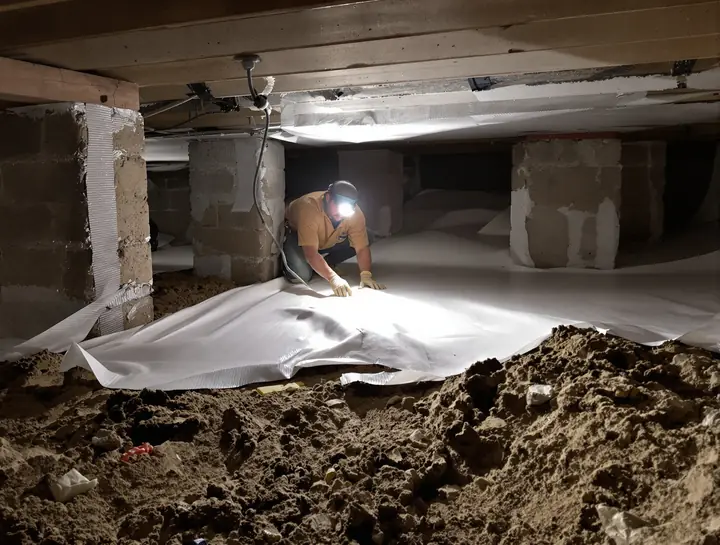 Worker laying a white vapor barrier in a crawl space