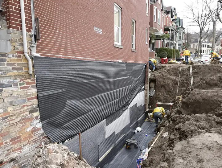 Crew sealing the outside of a foundation wall on a hillside