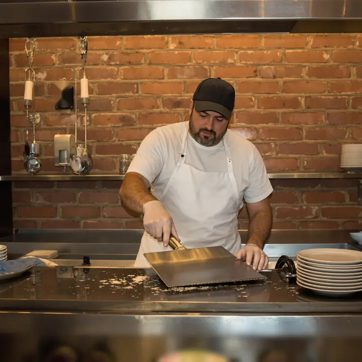 Diner owner scraping down the flat top grill between lunch and dinner