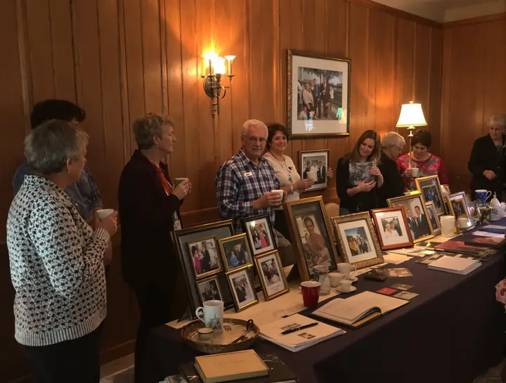 Friends talking beside a table of family photos at a memorial gathering