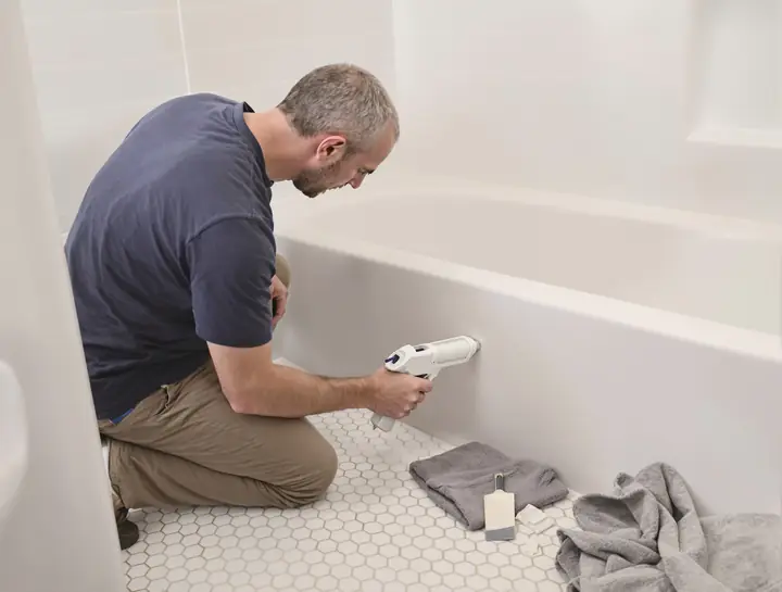 Handyman running a fresh bead of caulk around a white tub
