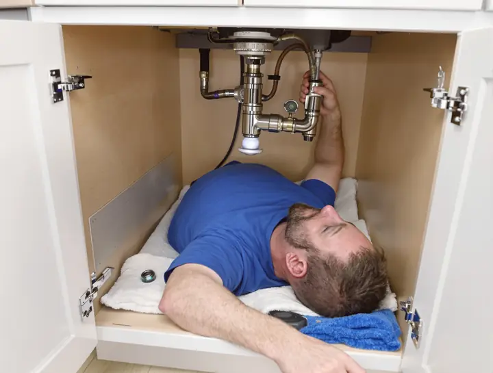 Handyman tightening a new kitchen faucet from under the sink