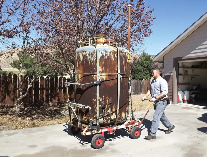 Installer rolling a rusted old tank down a Meridian driveway
