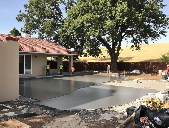 A crew pouring a new concrete patio behind a stucco home