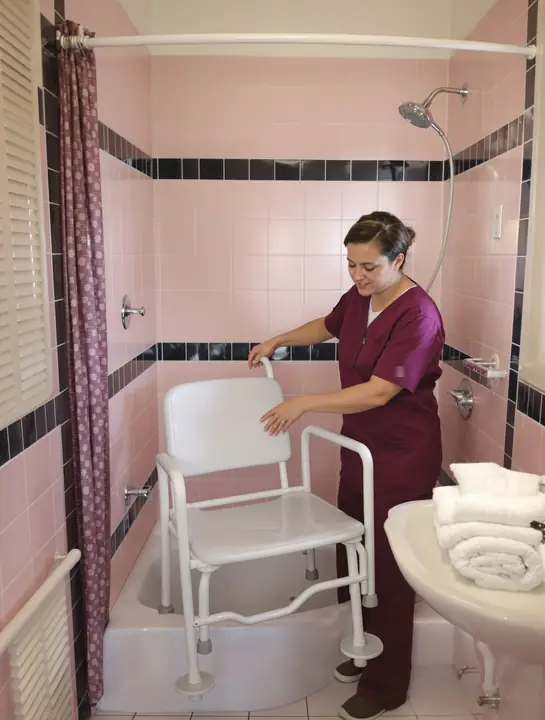 Caregiver setting up a shower chair in a pink tiled bathroom