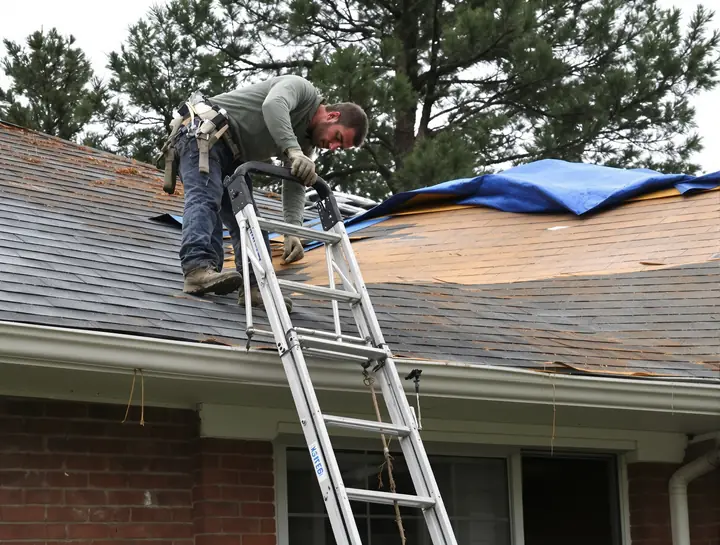 Roofer checking worn shingles and a tarp on a brick house