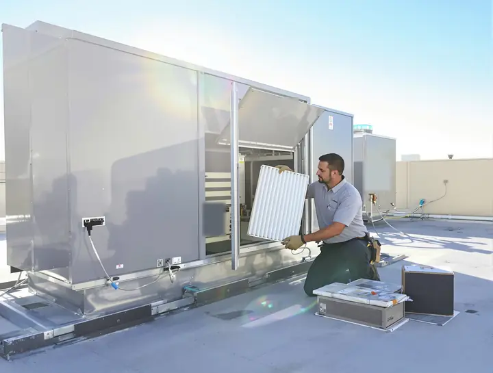 Technician sliding a new pleated filter into a rooftop unit