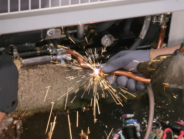 Tech brazing a copper refrigerant line on a condenser