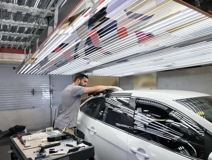 Dent repair tech pushing hail dents out of a sedan roof under a light board