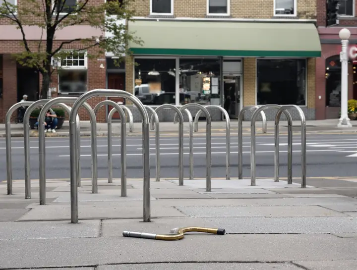 Cut bike lock on a Queens sidewalk next to an empty rack