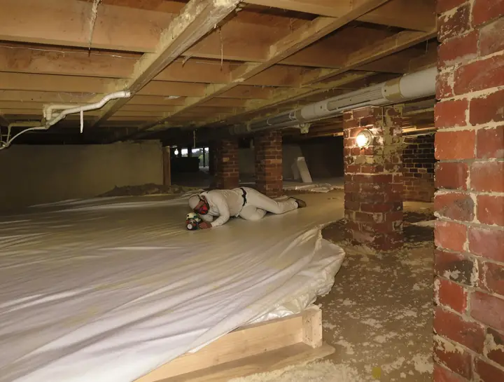 Installer spraying closed cell foam between floor joists in a crawlspace