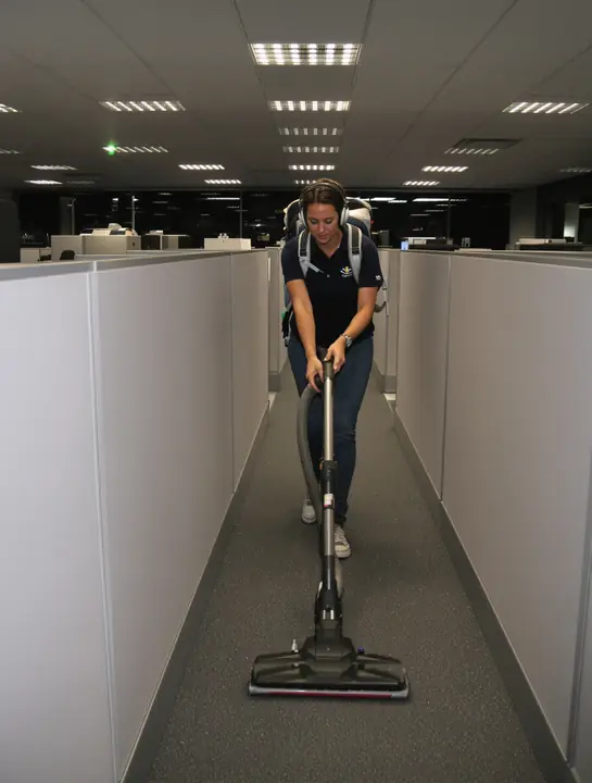 Cleaner with a backpack vacuum working under office desks at night