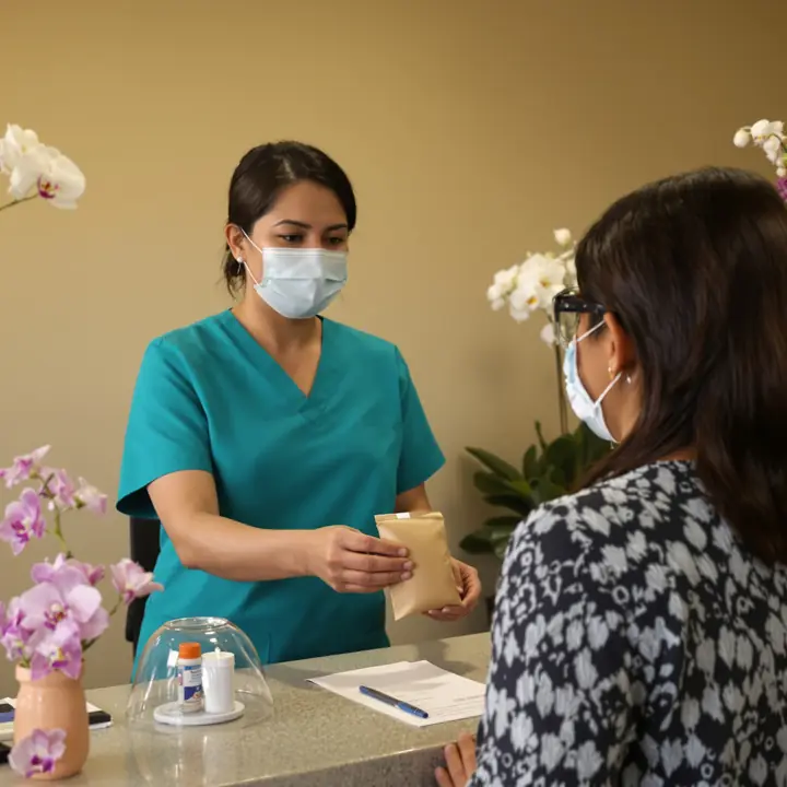 Staff handing a patient her eye drops and eye shields at the front desk