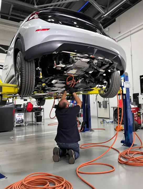 A tech checking the battery pack under an electric car