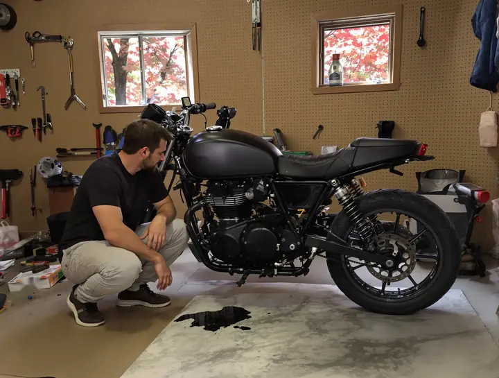 A rider looking at an oil spot under his new motorcycle in his garage