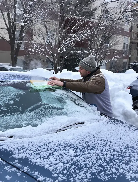 A man scraping ice off his sedan on a cold morning