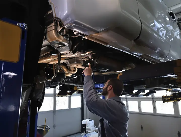 A technician checking a leak under a pickup truck on a lift in winter