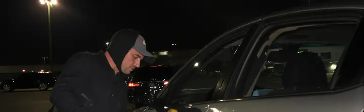 Locksmith at a car door in a parking lot at night