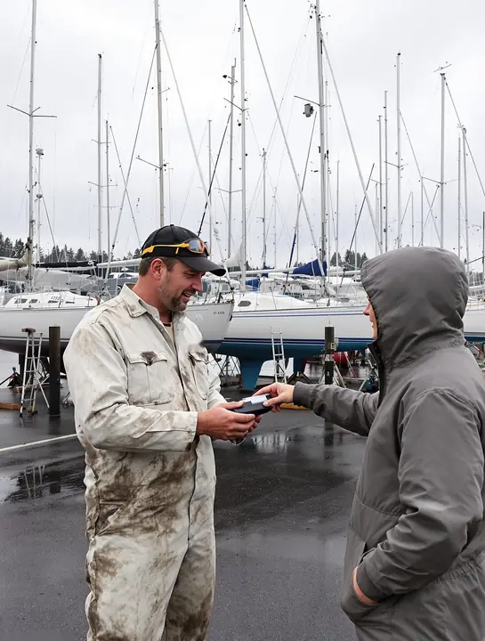 A marine mechanic handing a card reader to a boat owner at a Bellingham boatyard
