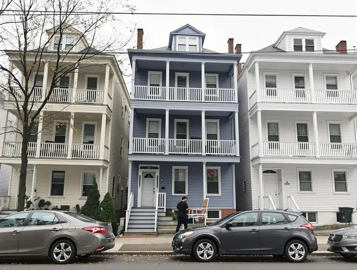 A hillside street of yellow, blue gray and white triple deckers in Worcester