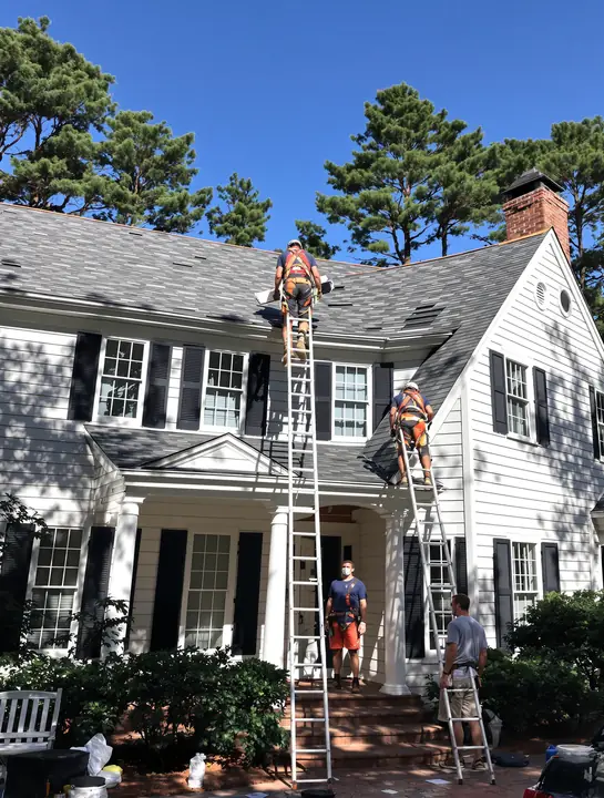 Roofers replacing shingles on a two story colonial