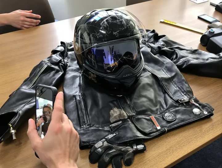 Scuffed helmet, torn jacket and gloves being photographed on a table